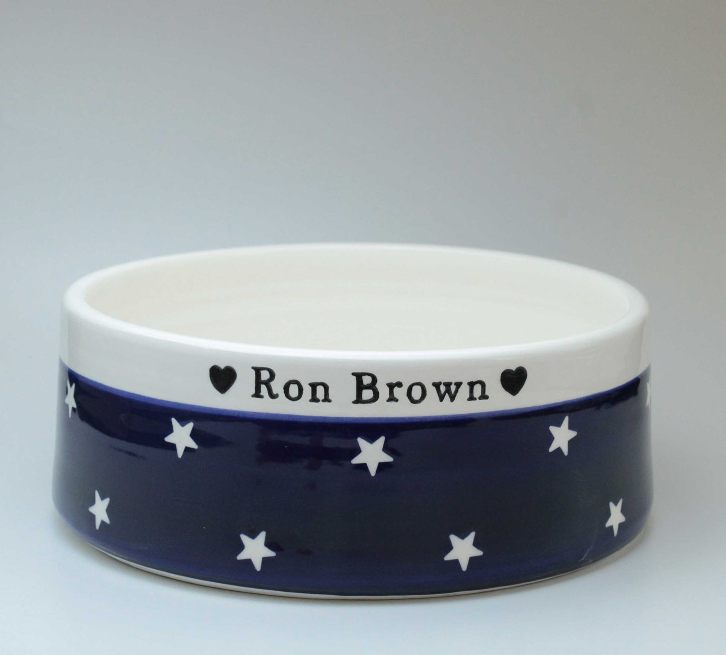 Navy blue ceramic bowl with white stars and 'Ron Brown' text on a gray background