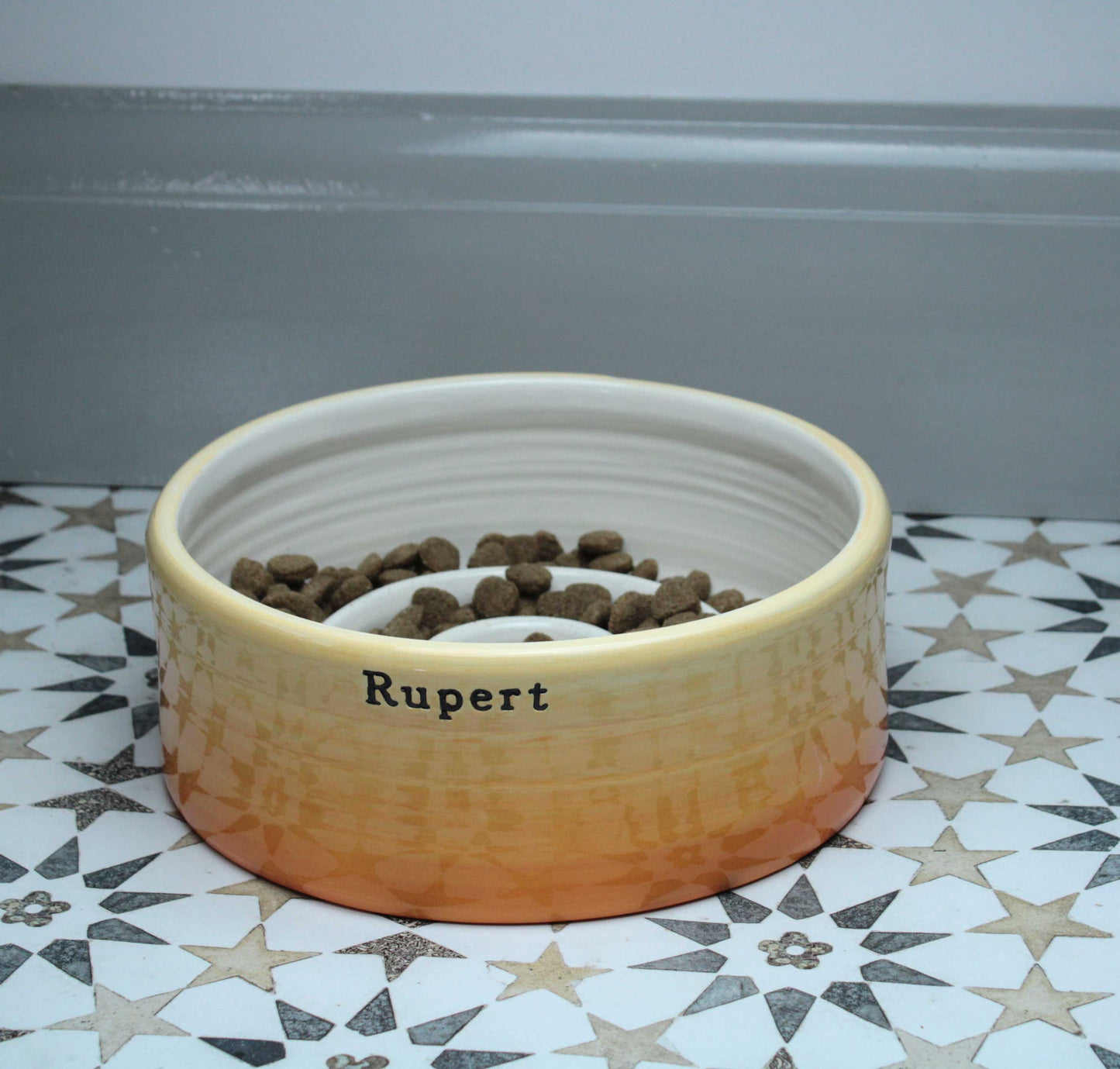 Ceramic pet bowl with 'Rupert' on a patterned floor