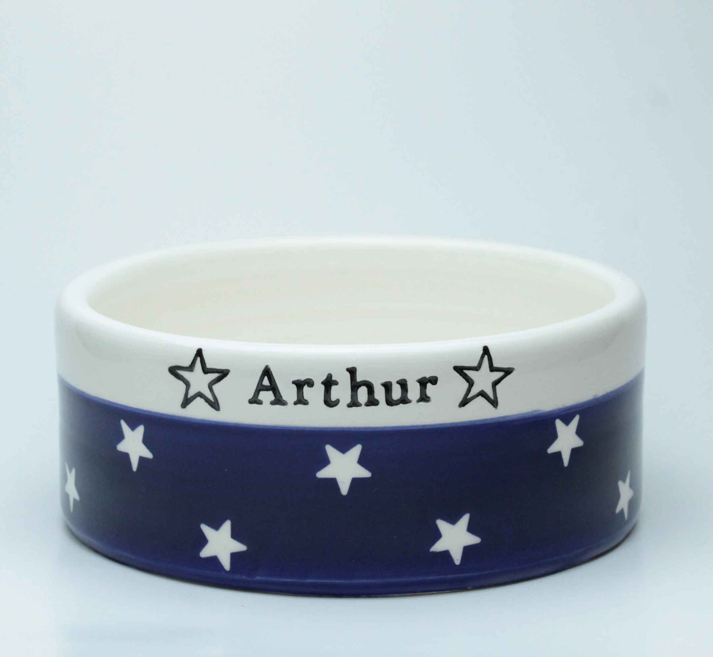 Ceramic bowl with blue band featuring white stars and 'Arthur' text on a white background