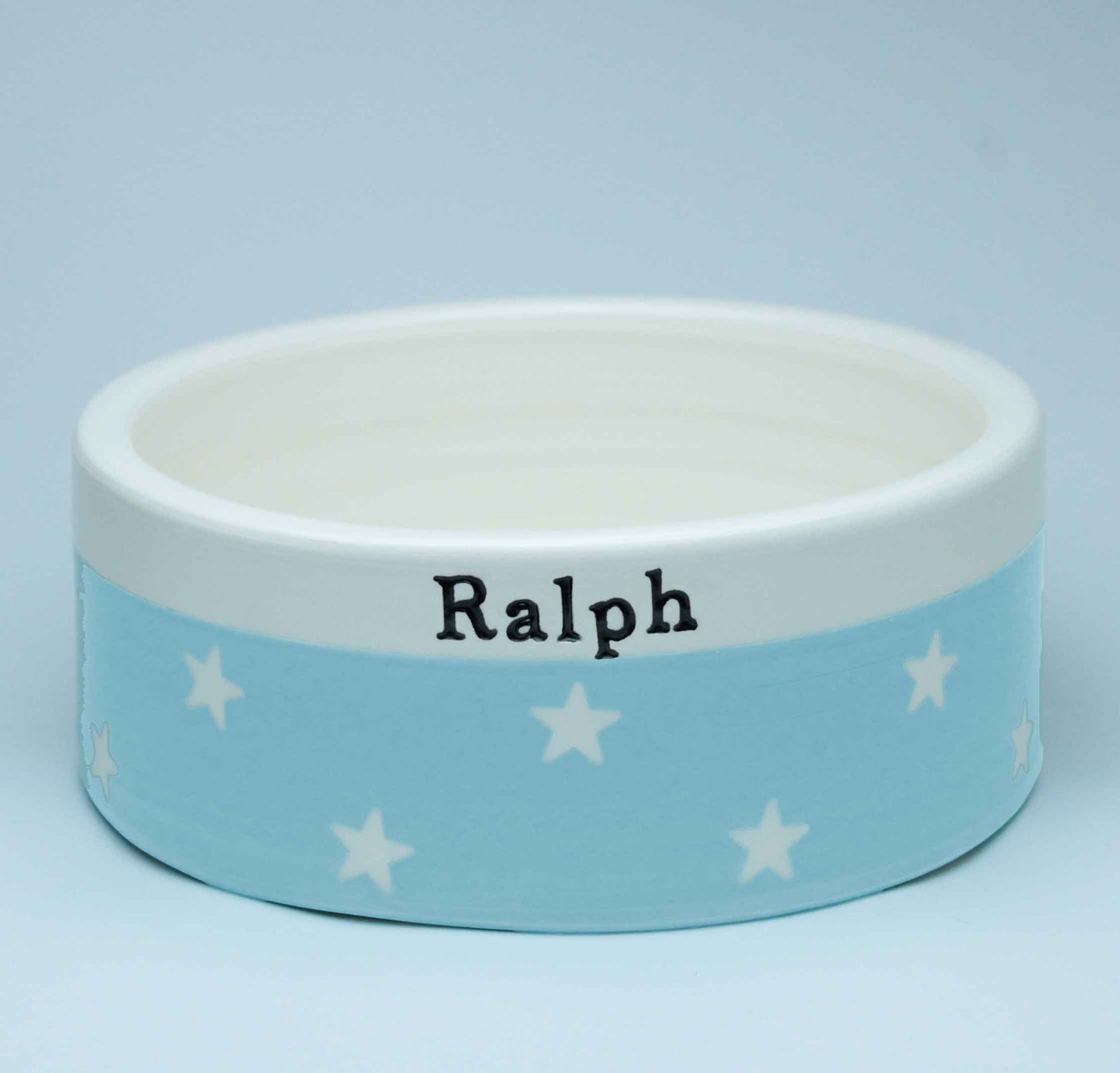 Dog bowl with 'Ralph' printed on it against a light blue background