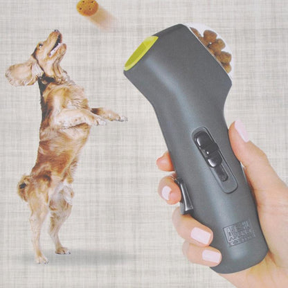 Hand holding a grey dog treat launcher  with a dog in the background