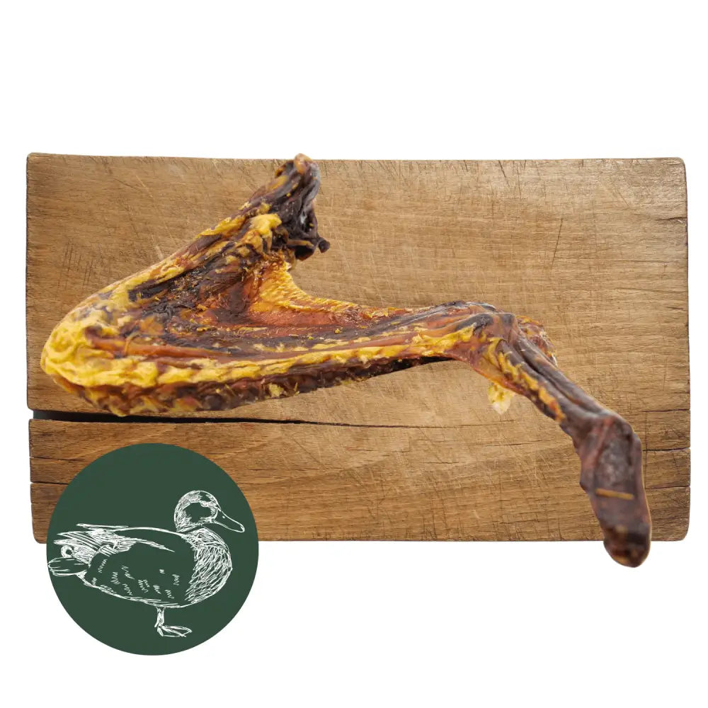 Dried duck leg on a wooden cutting board with a small green circle featuring a duck illustration.